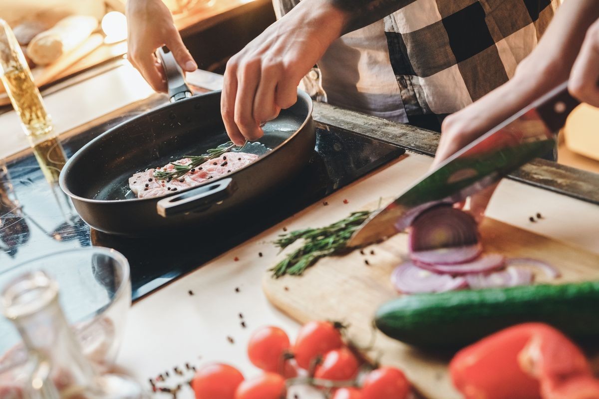 Closeup. Husband fries meat, wife cuts vegetable salad